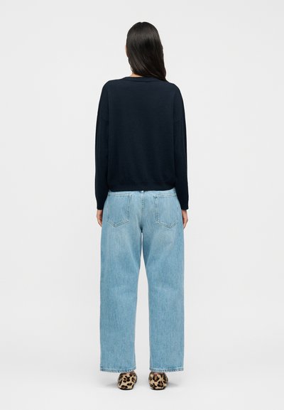 Μπλε πουλόβερ με άνετη εφαρμογή, συνδυασμένο με ανοιχτό μπλε τζιν παντελόνια φαρδιάς γραμμής. Το σύνολο ολοκληρώνεται με παπούτσια με λεοπάρ σχέδιο.