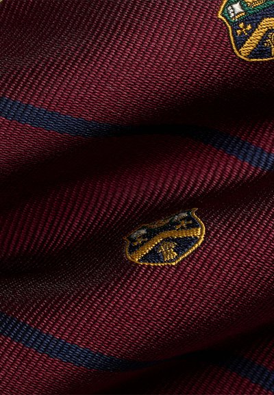 Tecido bordeaux com uma trama texturizada, apresentando riscas em azul-marinho e dois brasões bordados em tons de dourado e verde.