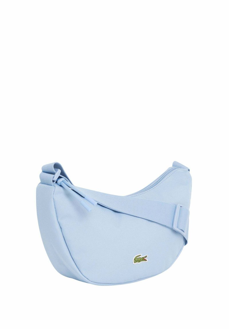 Sac d'épaule bleu clair en forme de croissant avec une bandoulière réglable et un petit logo de crocodile vert sur le devant.