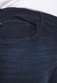 Vaqueros de mezclilla azul oscuro con un diseño clásico de cinco bolsillos, detalles cosidos y una textura suave cerca de la cintura.
