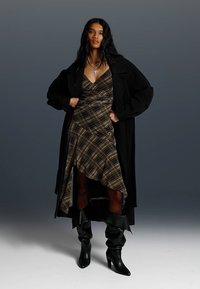 Karirana obleka z asimetričnim robom, nosena pod prevelikim črnim plaščem. V kombinaciji z črnimi škornji do kolen. Okrasek s srebrnim križem.