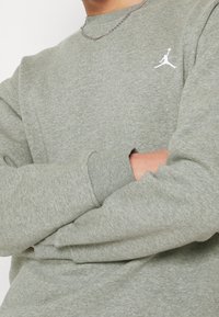 Felpa grigia realizzata in materiale morbido con scollo a girocollo, polsini a coste e logo Jordan bianco sul petto.