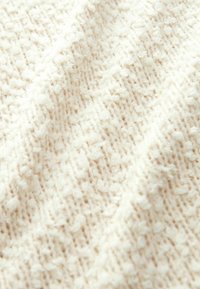 Tissu texturé couleur crème avec une apparence douce et duveteuse, présentant un motif subtil et un design tissé. Idéal pour des applications en tricot.