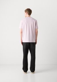 Lyserød T-shirt med korte ærmer og rund hals, båret med sorte jeans og lyse sneakers, set fra ryggen.