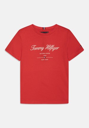 Czerwona bawełniana koszulka z krótkim rękawem z białym napisem „Tommy Hilfiger Established 1985 New York” i małym logo na lewym rękawie.