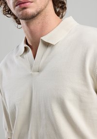 Light beige polo shirt with a soft texture, short sleeves, and a notched collar design. The fabric appears breathable and casual.