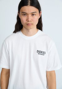 Balta trumpa rankovė T-marškiniai su juodu "Dickies Workwear" logotipu kairėje krūtinės pusėje. Pagaminta iš lygaus medvilnės audinio.