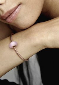 Bracciale in oro rosa con un dettaglio a perla liscia di colore rosa. Il design presenta una texture attorcigliata lungo il bracciale, appoggiato su una tonalità di pelle chiara.