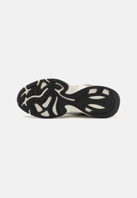 Semelle d'une basket avec un motif noir et blanc et le nom de la marque Michael Kors embossé près de la zone du talon.