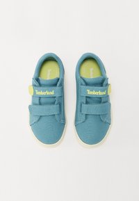 Modré plátěné tenisky s páskem na suchý zip a žlutými akcenty. Kulatá špička a bílá gumová podrážka. Na pásku je uvedeno jméno značky "Timberland".