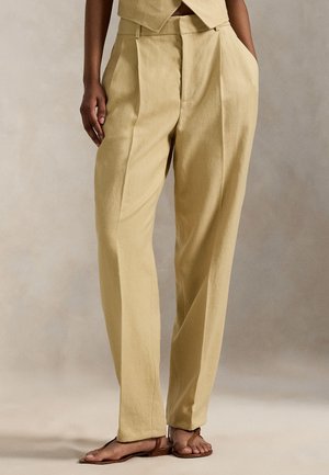 Jasnożółte lniane spodnie o luźnym kroju, z zakładkami, bocznymi kieszeniami i wysokim stanem. W połączeniu z brązowymi sandałami.