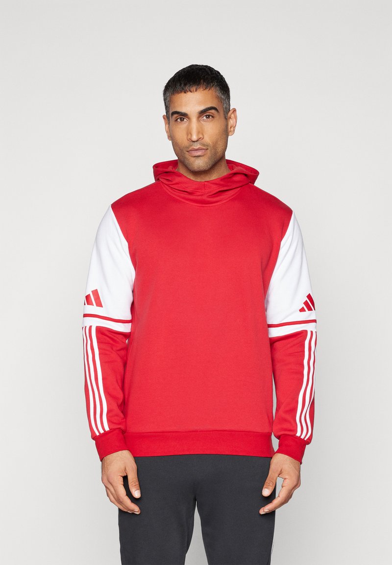 Röd sweatshirt med högt halsliv, med vita ärmar och tre vita ränder på varje arm. Materialet verkar mjukt och strukturerat.