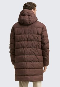 Brauner Puffer-Mantel mit Kapuze, der gesteppten Abschnitte und einen knielangen Saum hat. Hergestellt aus strukturiertem Stoff mit matter Oberfläche.