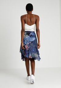 Luftig blå blommig kjol med lager på lager volangkant, matchad med vit satinlinne. Modellen bär vita sneakers.