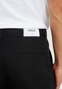 Zwarte broeken met een gladde textuur, voorzien van een wit label met "FARAH" op de achterkant van de tailleband en een platte achterzak.