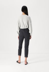 Maglione grigio oversize in tessuto testurizzato abbinato a pantaloni in denim grigio scuro a tre quarti. I pantaloni presentano tasche posteriori e orli risvoltati.