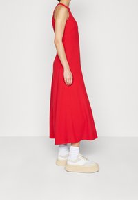 Robe midi sans manches rouge avec une silhouette évasée, présentant une texture lisse. Associée à des baskets blanches imposantes et des chaussettes blanches mi-mollet.