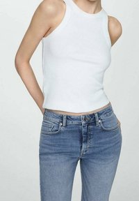 Valkoinen ribattu hihaton paita yhdistettynä sinisiin farkkuihin. Farkuissa on klassinen malli, jossa on etutaskut ja vetoketjukiinnitys.