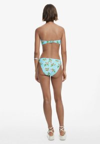 Kvetinový bikiny set s svetlo modrým pozadím, nastaviteľnými popruhmi s sponou a zodpovedajúcimi vysokými nohavičkami so podobným vzorom.