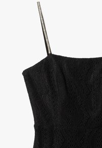 Zwarte kanten jurk met golvend patroon, met een rechte halslijn en slanke bandjes versierd met rhinestones. Textuurdetail van de stof zichtbaar.