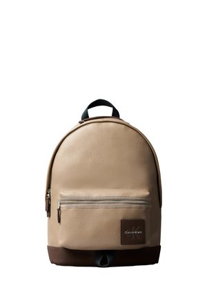 Beige leather backpack with front zip pocket, dark brown base, black handle, and Calvin Klein logo patch on front pocket.