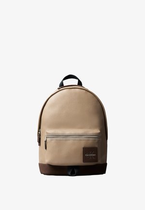 Beige læderrygsæk med lynlåslomme foran, mørkebrun bund, sort håndtag og Calvin Klein-logo på frontlommen.