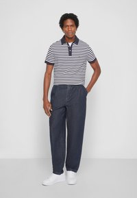 Stripet polo skjorte i marineblå og hvid, med korte ærmer og krave; parret med mørk denim bukser og hvide sneakers.