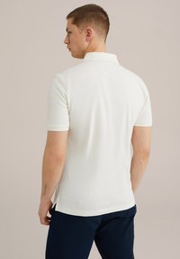 Bílá polo košile z bavlněného směsového materiálu, s krátkými rukávy, skládacím límcem a bočními rozparky, spárovaná s námořnickými kalhotami.