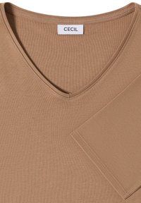Chemise marron à manches courtes avec col en V montrant l'encolure, les coutures et l'étiquette de la marque CECIL à l'intérieur du col.