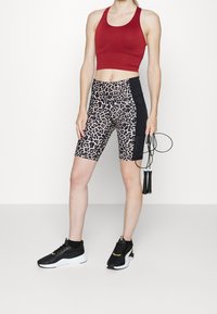 Czerony stanik sportowy, szorty rowerowe w zwierzęcy wzór z czarnym bocznym panelem oraz czarne sneakersy z białymi podeszwami i złotymi akcentami. Skakanka w ręku.
