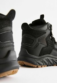 Czarne sneakersy typu high-top z panelami z zamszu i siateczki, teksturowanymi gumowymi podeszwami, wzmocnionymi czubkami oraz sznurowanym designem.