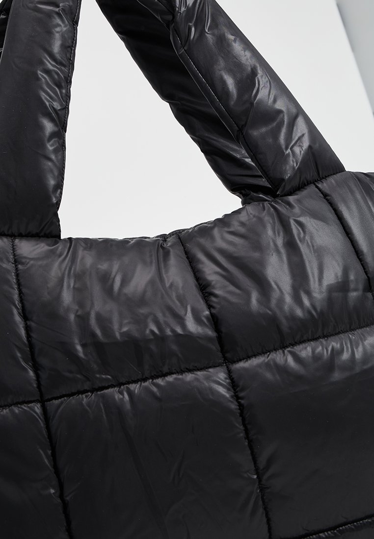 Schwarze, gesteppten Tasche mit gepolstertem Design, aus glattem, glänzendem Material und dicken, weichen Griffen für einfaches Tragen.