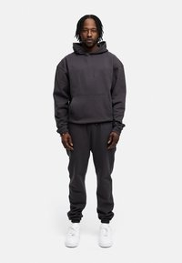 Dunkelgrauer Hoodie mit einer Fronttasche, kombiniert mit dunkelgrauen Jogginghosen. Besitzt elastische Bündchen und weiße Sneakers. Glatte Stofftextur.