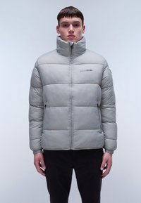 Ljusgrå vadderad jacka med hög krage och frontdragkedja. Har sömnadsinsatser och sidofickor. Tillverkad av ett slätt, glänsande material.