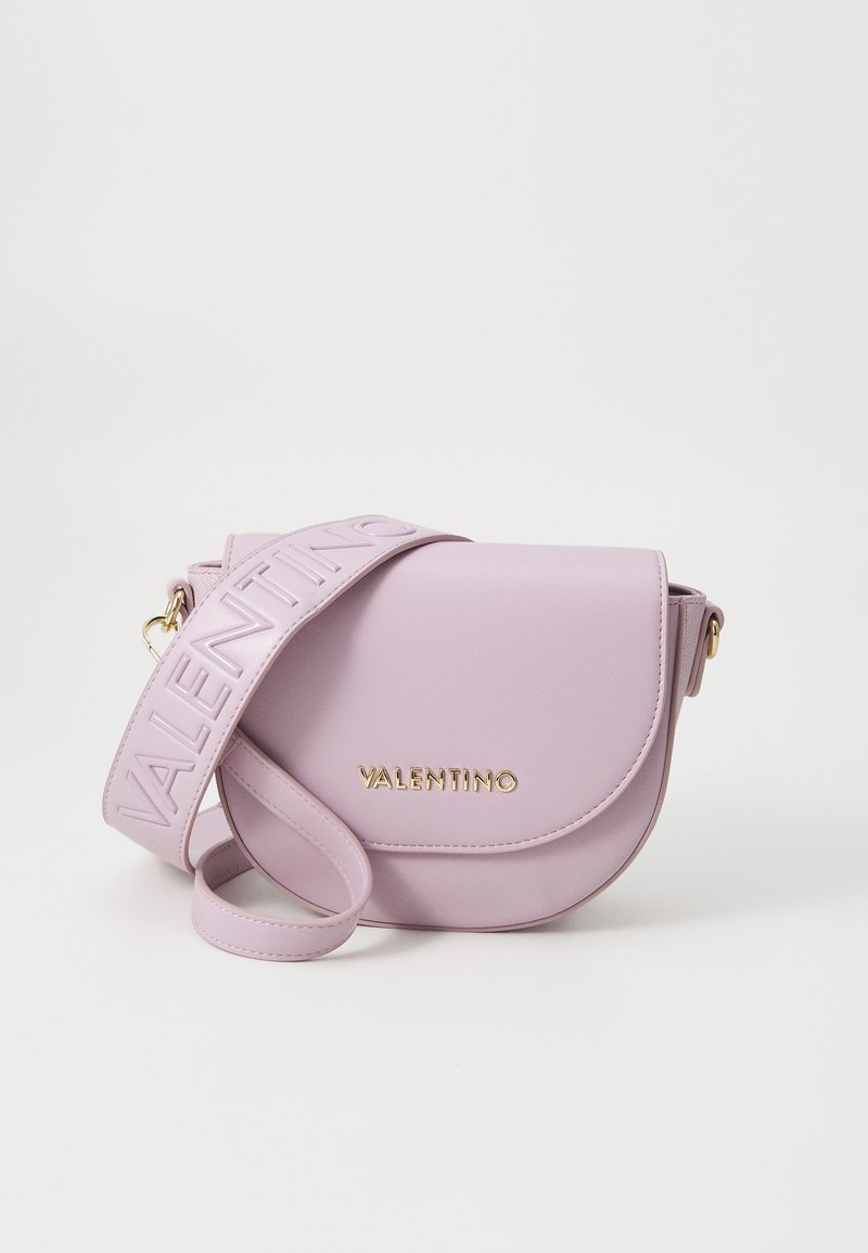 Purpura ādas crossbody soma ar izliekta formu, zelta furnitūru un platām siksnām, uz kurām ir iegravēts "VALENTINO" logo.