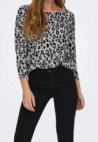 Leopardmuster-Pullover in Grau und Schwarz, mit Rundhalsausschnitt und drei Viertelärmeln, kombiniert mit schwarzen, eng anliegenden Jeans.