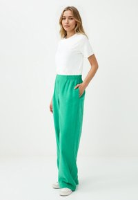 Witte katoenen t-shirt met korte mouwen gecombineerd met losvallende, levendige groene broek met een elastische tailleband en zijzakken. Sneakers inbegrepen.