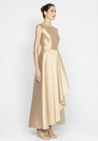 Suknia z satyny w kolorze złotym, sięgająca do podłogi, z dopasowanym gorsetem, delikatnie rozkloszowanym dołem i drapowanym brzegiem. W komplecie z odsłoniętymi szpilkami w kolorze nude.