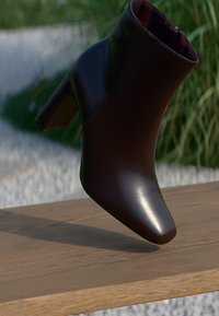 Shiny black leather ankle boot with block heel resting on a wooden surface against a blurred outdoor background.