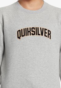 Gray sweatshirt featuring a round neckline, long sleeves, and a black and orange "QUIKSILVER" logo arching across the chest.