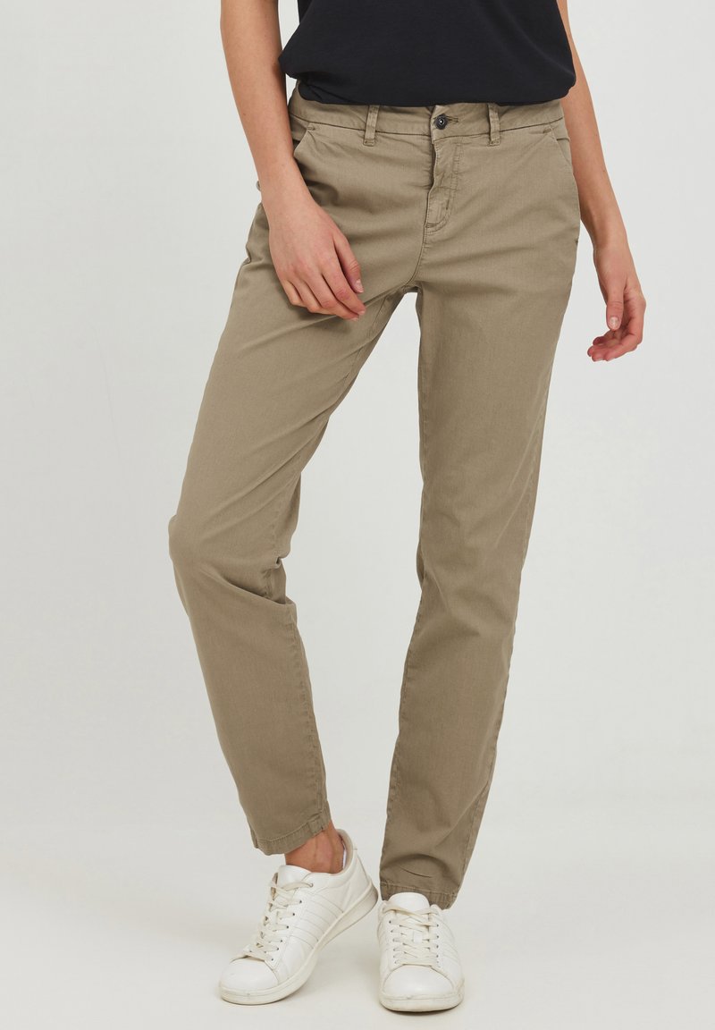 Chino beige con una vestibilità slim, dotati di chiusura con bottone e zip, tasche laterali e leggera tapered alla caviglia. Abbinati a sneaker bianche.