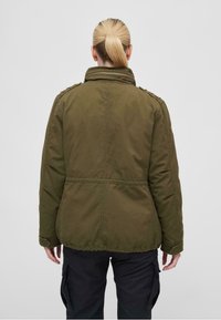 Chaqueta de algodón verde con alto cuello, cierre frontal con cremallera y hombreras. Cuenta con dobladillo y mangas elásticos, y tejido texturizado.