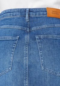 Blå denimkjol med synlig sömnad, två bakfickor och en ljusbrun läderlapp med texten "TOMMY HILFIGER" vid midjan.