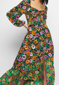 Abito maxi floreale con maniche lunghe, caratterizzato da un vivace motivo di fiori rosa, arancioni e verdi su uno sfondo nero, e uno spacco laterale.