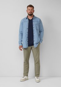 Jasnoniebieska jeansowa koszula na granatowym t-shircie z dekoltem w serek, połączona z oliwkowymi spodniami i białymi trampkami. Prosty, casualowy design i fason.