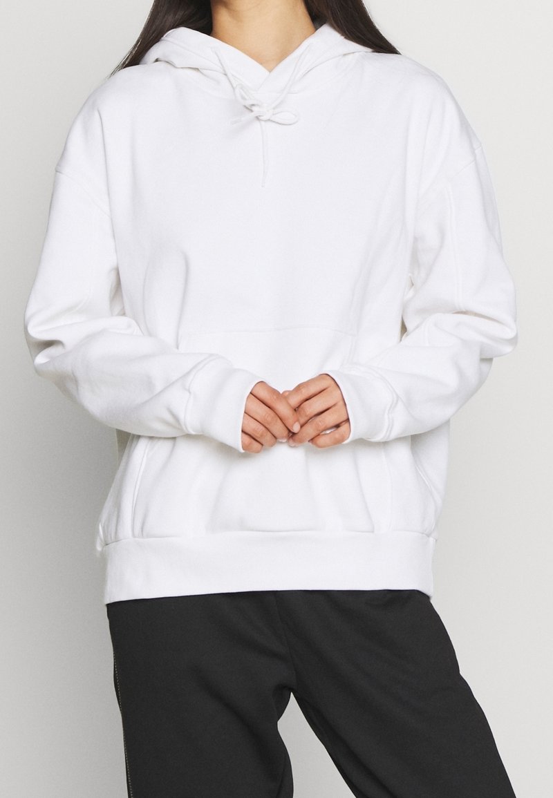 Witte hoodie met trekkoord, kangoeroezak en ribgebreide manchetten. De stof lijkt zacht met een gladde textuur. Vooraanzicht.