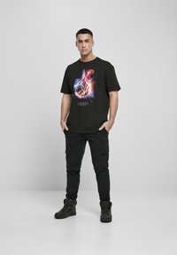 Sort T-shirt med en farverig grafisk print på forsiden. Sammen med sorte cargo-bukser og sorte høje sneakers.