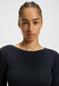 Top noir en tricot côtelé avec un col bateau et un motif perforé subtil, mettant en avant un design ajusté et des manches longues.