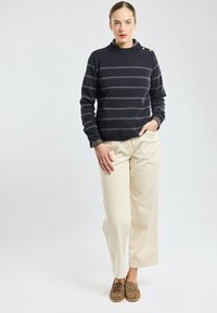 Maglioncino a righe navy con collo alto e dettagli a bottoni, abbinato a pantaloni beige a gamba larga e scarpe slip-on con stampa leopardata.