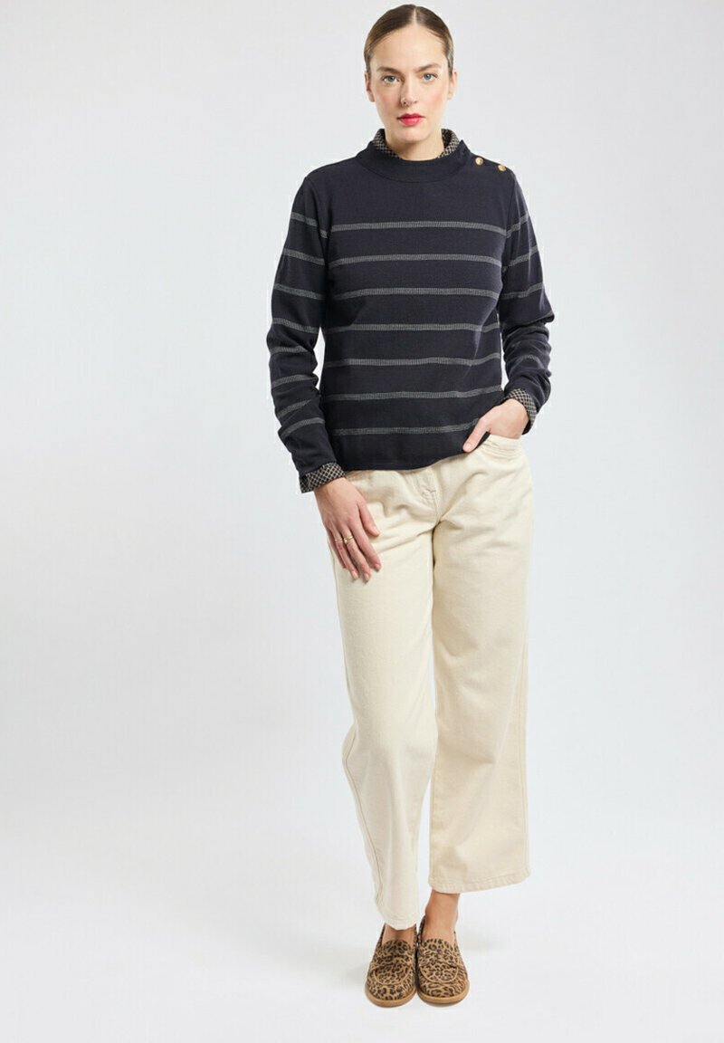 Maglioncino a righe navy con collo alto e dettagli a bottoni, abbinato a pantaloni beige a gamba larga e scarpe slip-on con stampa leopardata.